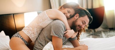 Frau in Unterwäsche umarmt Partner auf dem Bett