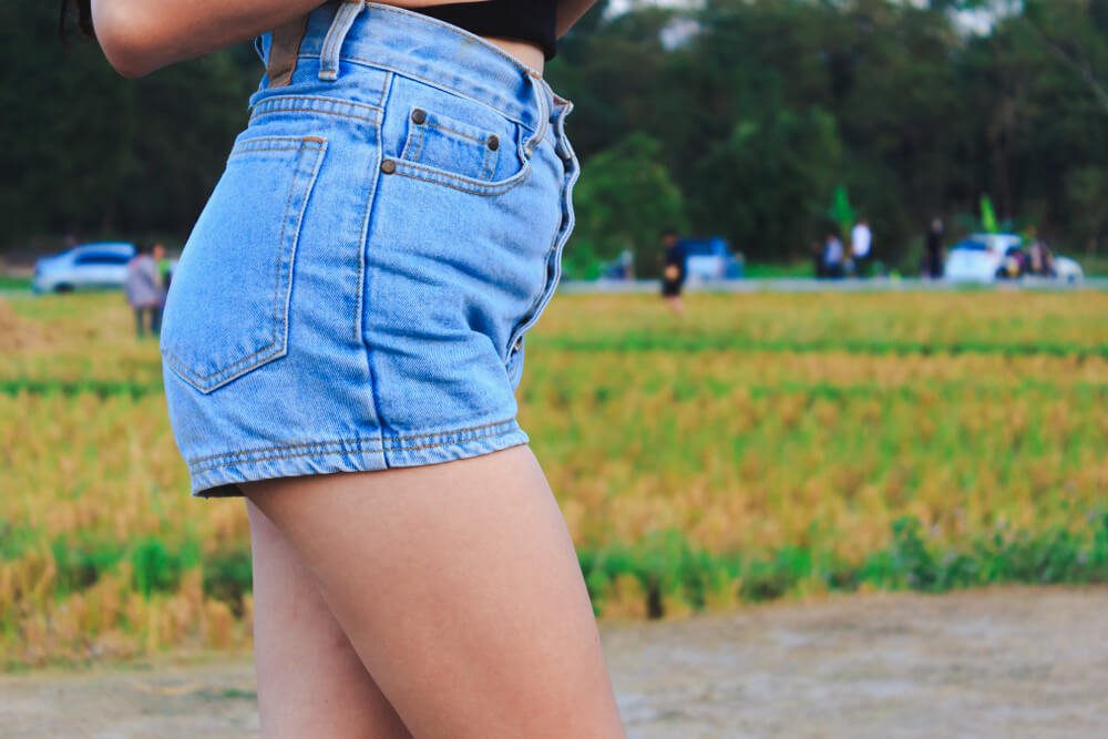 Frau in kurzer Jeansshorts läuft an einem Feld vorbei
