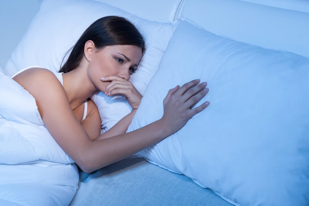 Frau liegt traurig alleine im Bett mit Hand auf dem Kopfkissen neben ihr