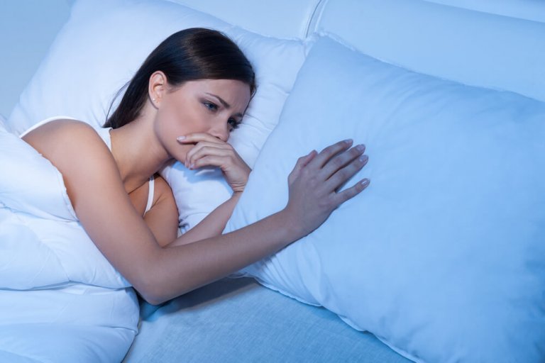 Frau liegt traurig alleine im Bett mit Hand auf dem Kopfkissen neben ihr