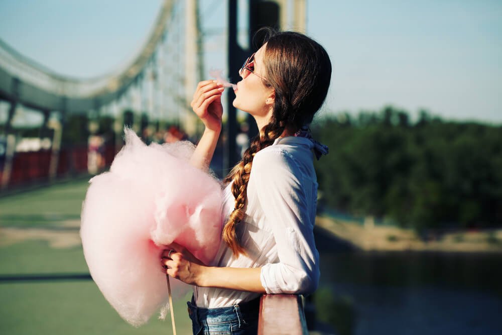 Frau steht draußen auf einer Brücke und isst Zuckerwatte