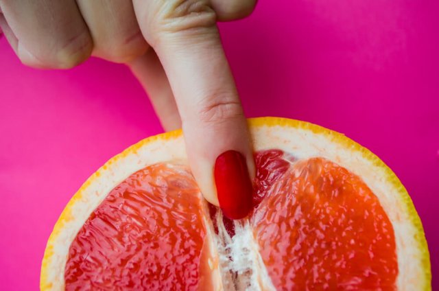 Eine Frau mit rot lackiertem Nagel deutet mit dem Mittelfinger auf die Mitte einer aufgeschnittenen Grapefruit