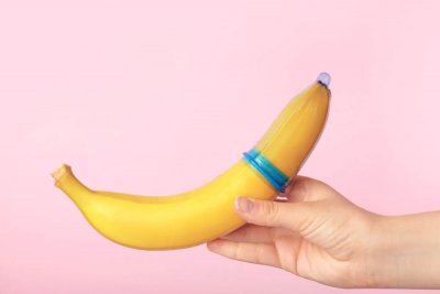 Eine Frau hält eine Banane über die ein blaues Kondom gestülpt ist