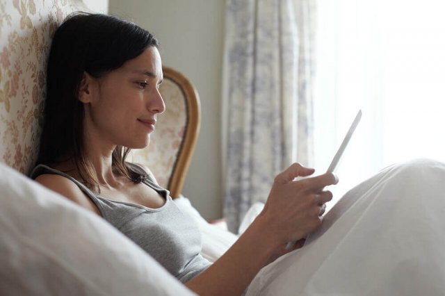 Eine Frau liegt im Bett und liest etwas auf einem Tablet