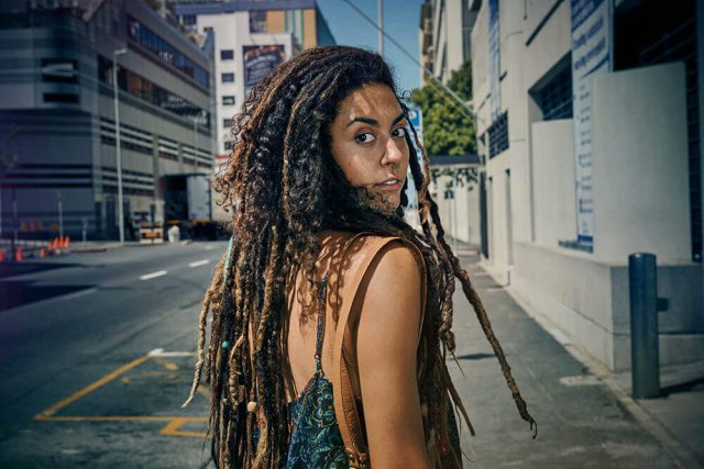 Eine Frau mit Dreadlocks läuft auf der Straße, sie schaut über ihre Schulter zurück