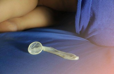 Ein benutztes Kondom liegt auf einem Bett, im Hintergrund sind die Beine einer Frau zu sehen