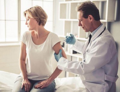 Ein Arzt spritzt einer Frau in den Arm, sie schaut zur anderen Seite