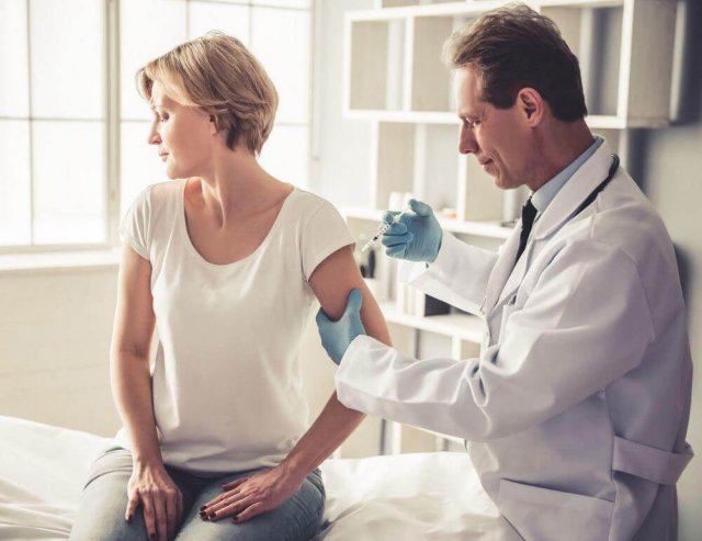 Ein Arzt spritzt einer Frau in den Arm, sie schaut zur anderen Seite